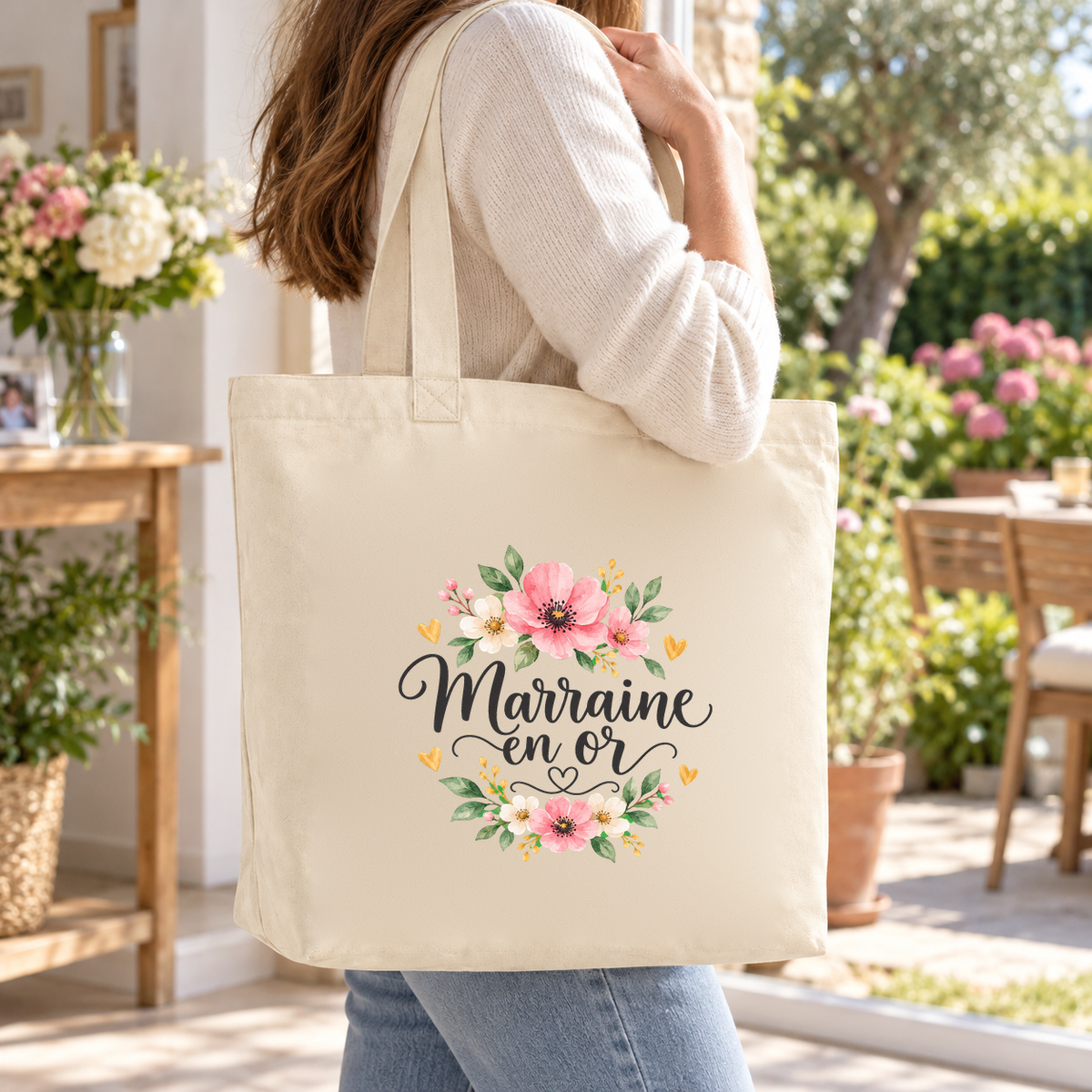 Tote bag marraine « Marraine en or » Premium porté à l'épaule sur une terrasse fleurie, lors d'une promenade au jardin