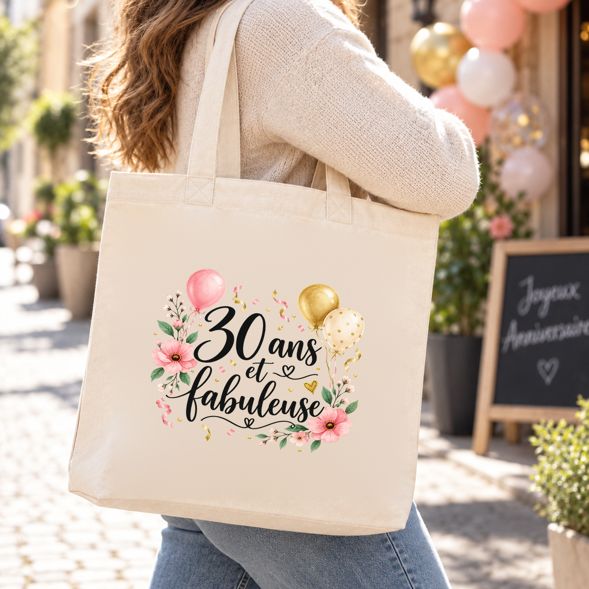 Tote bag anniversaire « 30 ans et fabuleuse » Premium porté à l'épaule dans une rue ensoleillée décorée de ballons