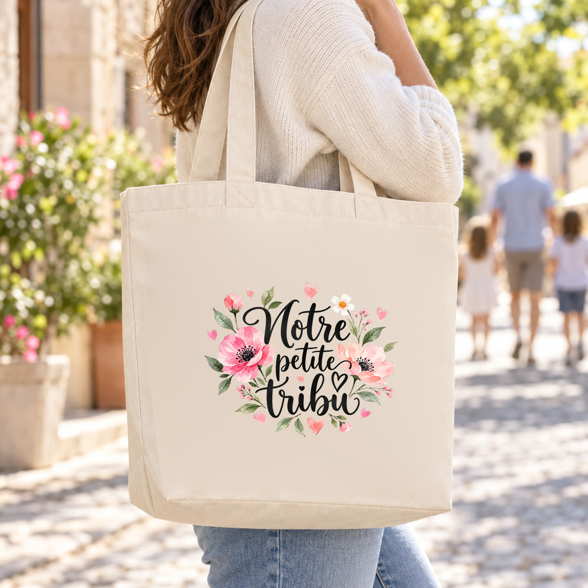 Tote bag famille « Notre petite tribu » Premium porté à l'épaule dans une rue ensoleillée, lors d'une promenade en famille