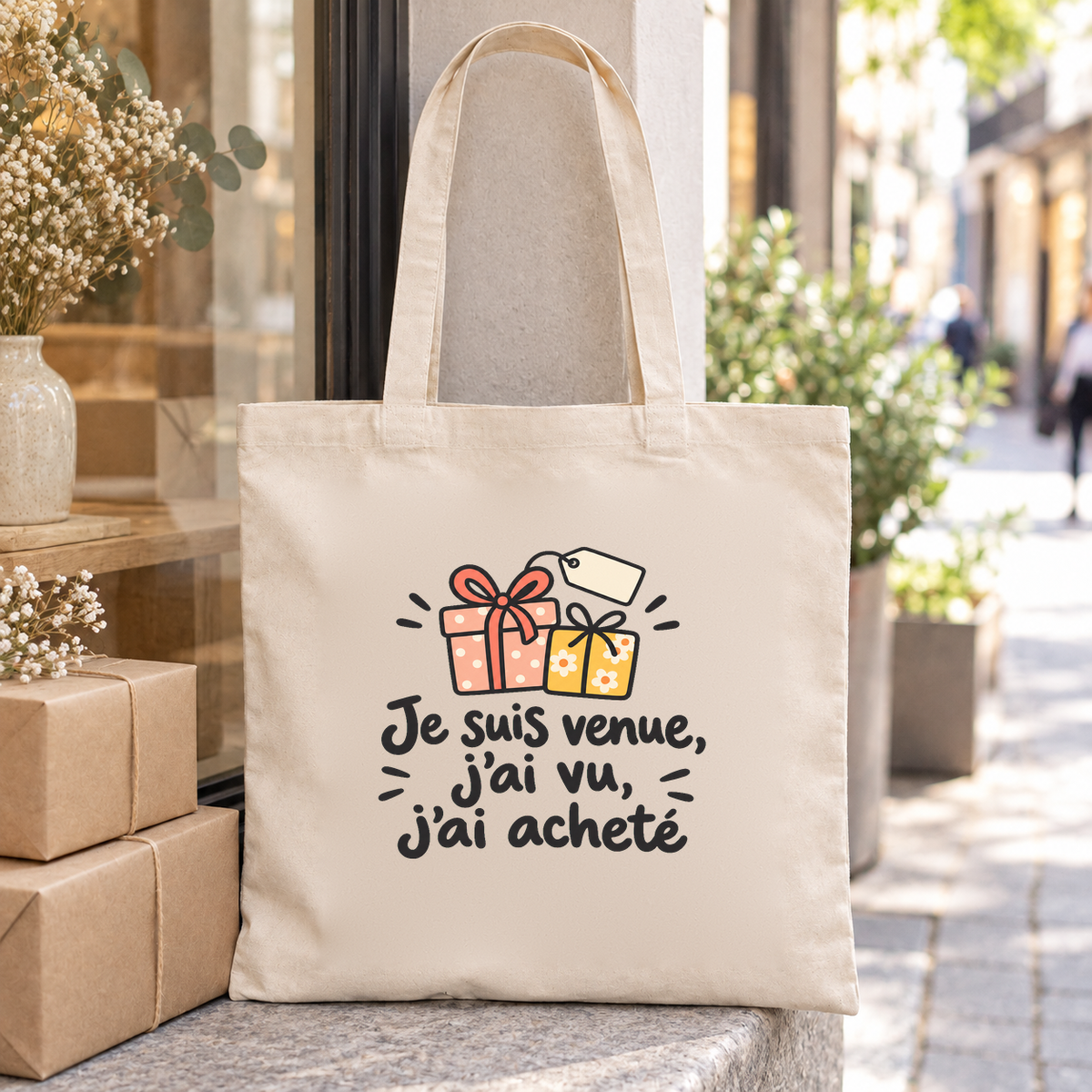 Tote bag « Je suis venue, j'ai vu, j'ai acheté » Essentiel posé sur des paquets en papier kraft dans une rue commerçante