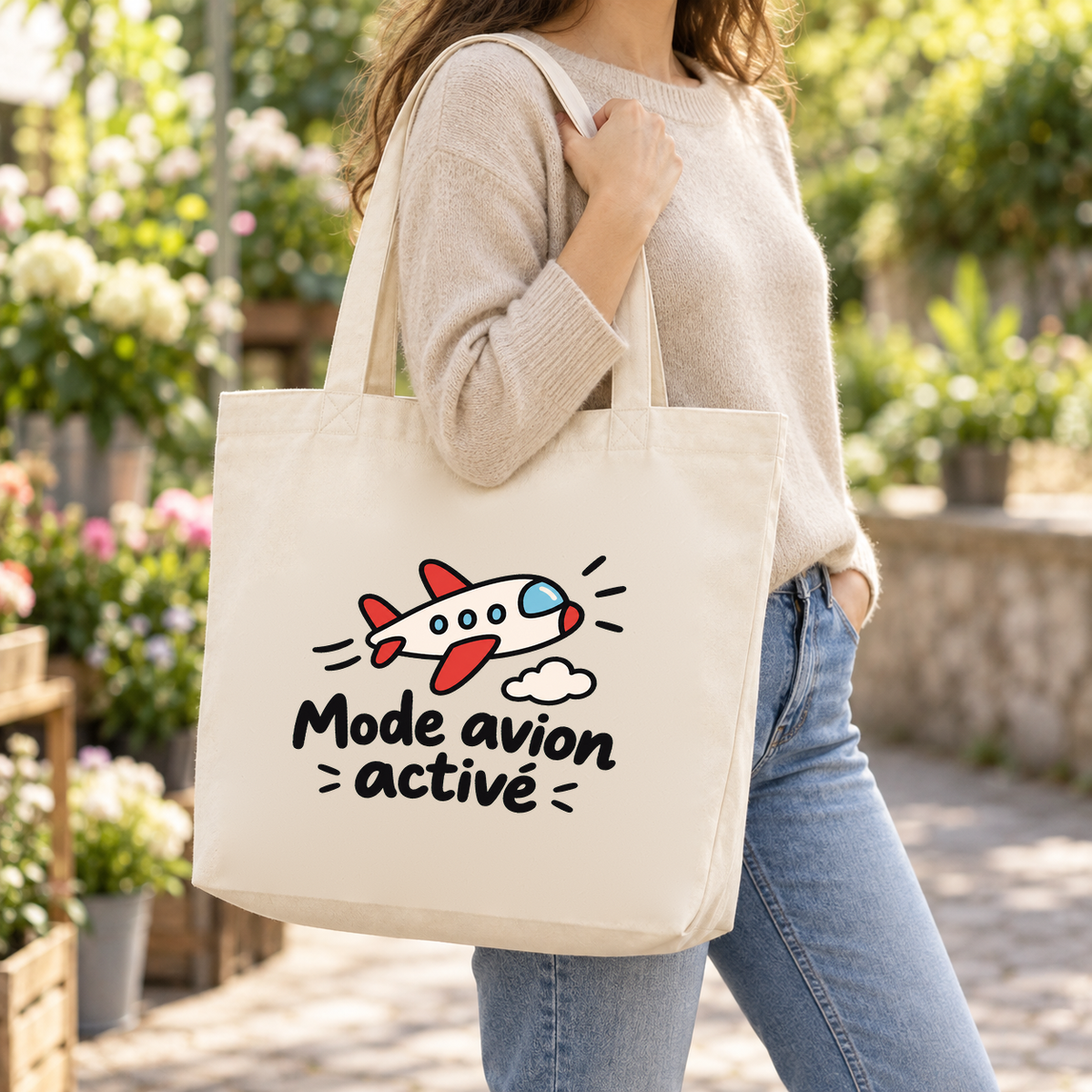 Tote bag « Mode avion activé » Premium porté à l'épaule dans une ruelle fleurie