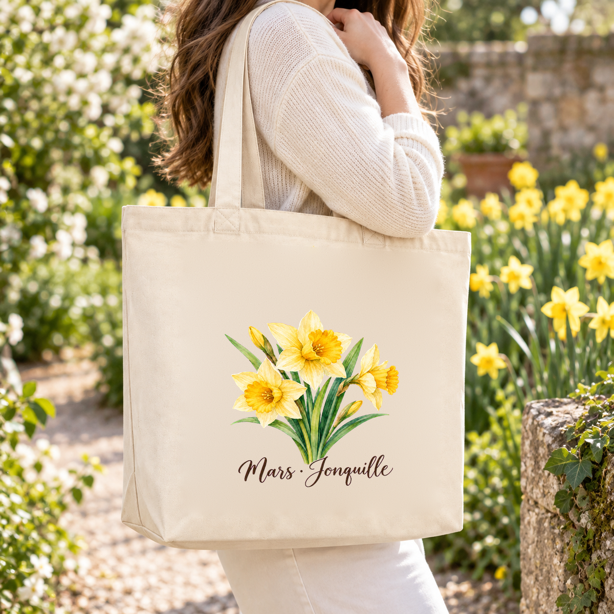 Tote bag fleur de naissance « Mars · Jonquille » Premium porté à l'épaule dans un jardin fleuri de jonquilles