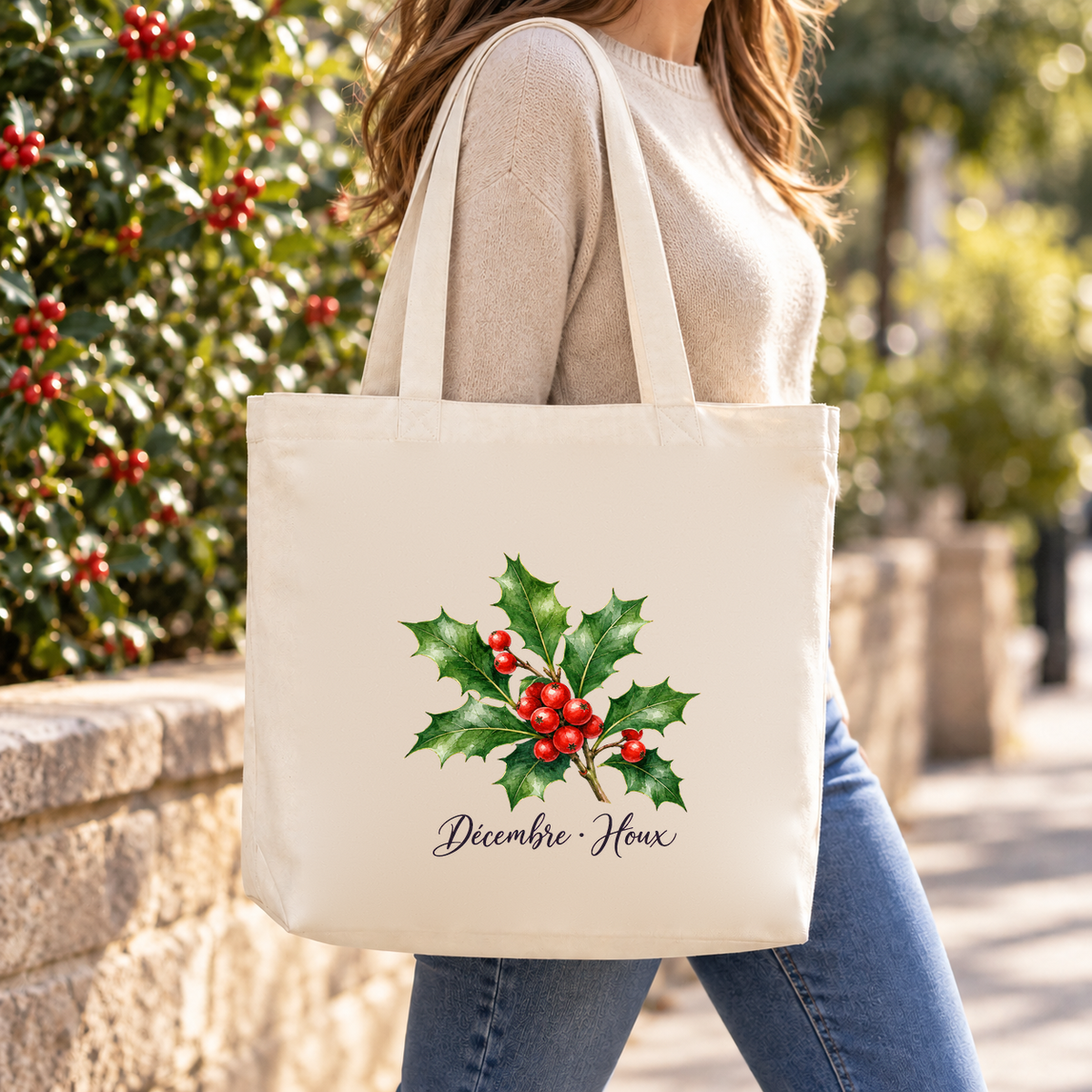 Tote bag fleur de naissance « Décembre · Houx » Premium porté à l'épaule dans une rue bordée de houx