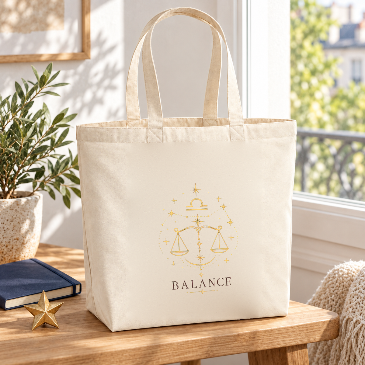 Tote bag signe astrologique « BALANCE » Premium posé sur une table près d'une fenêtre, à côté d'un carnet et d'une petite étoile dorée