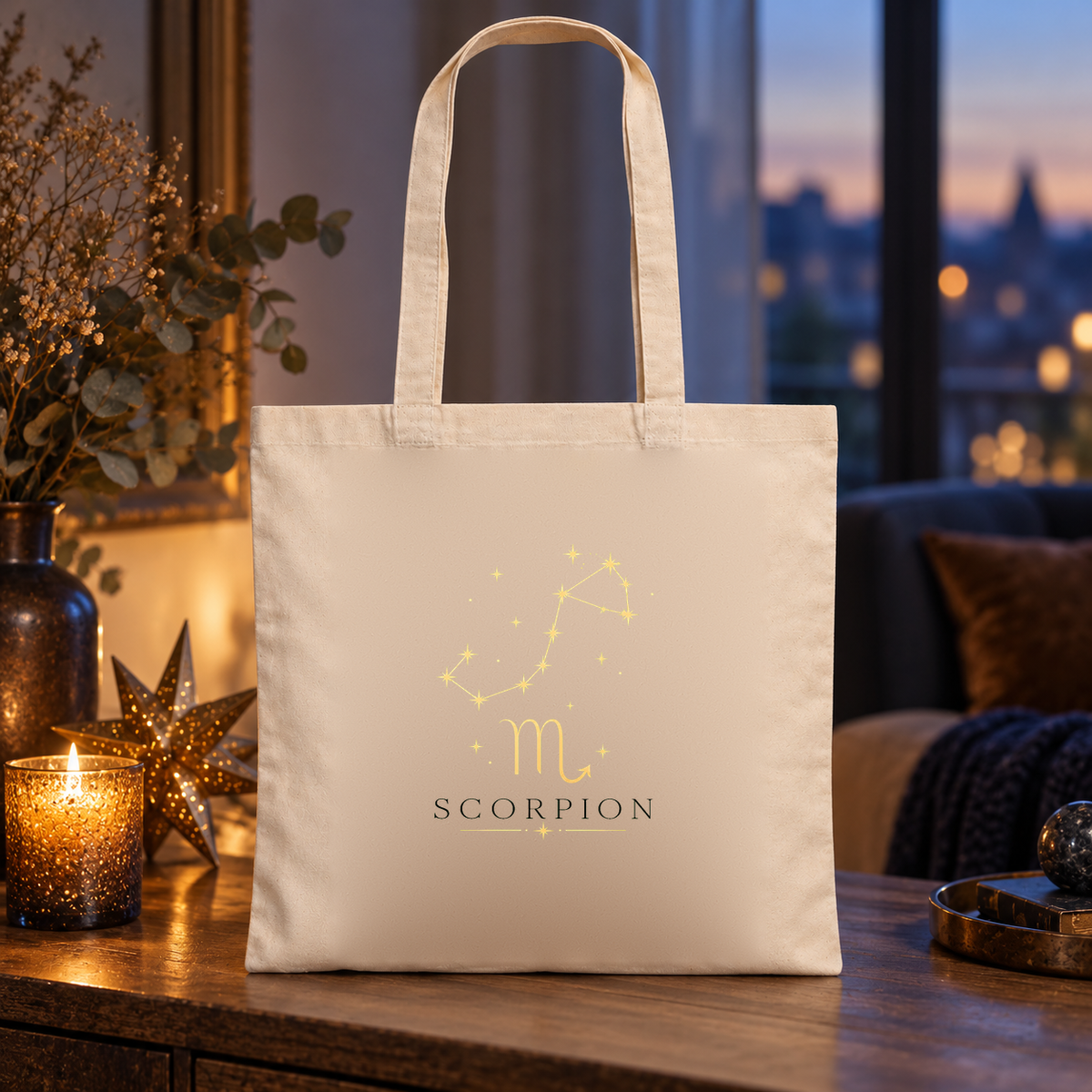 Tote bag signe astrologique « SCORPION » Essentiel posé sur une table près d'une fenêtre, à côté de bougies et d'une étoile dorée, à la tombée de la nuit