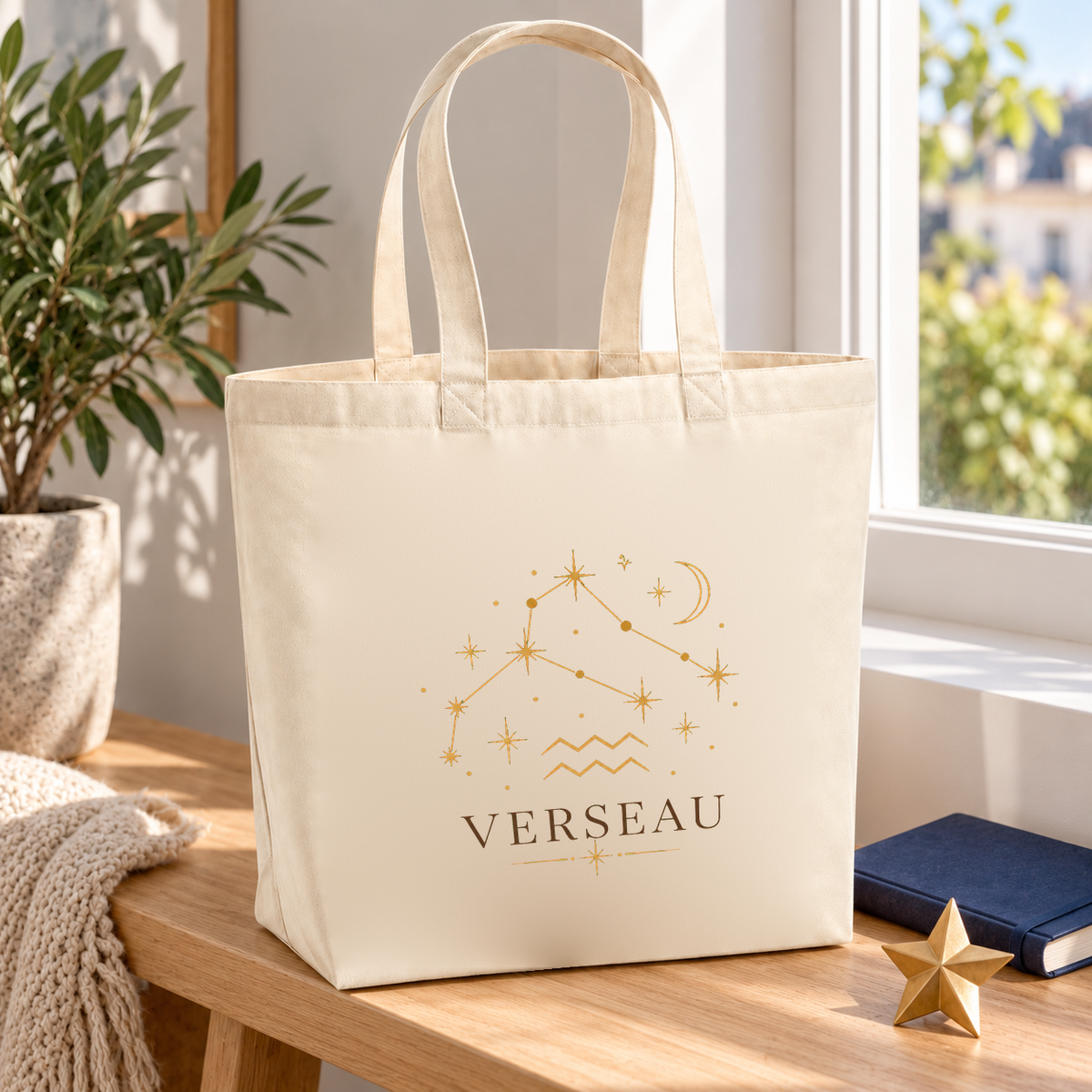 Tote bag signe astrologique « VERSEAU » Premium posé sur une table près d'une fenêtre, à côté d'un carnet et d'une petite étoile dorée