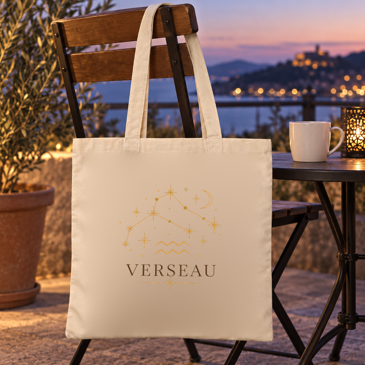 Tote bag signe astrologique « VERSEAU » Essentiel suspendu à une chaise de terrasse face à la ville au crépuscule
