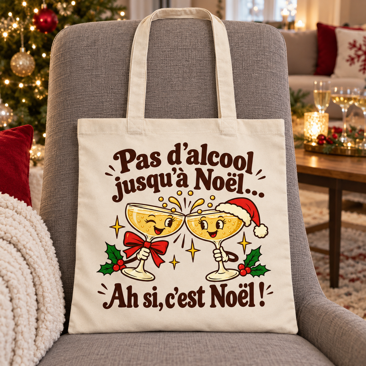 Tote bag Noël « Pas d’alcool jusqu’à Noël… Ah si, c’est Noël ! » Essentiel posé contre le dossier d'une chaise, décor de Noël en arrière-plan