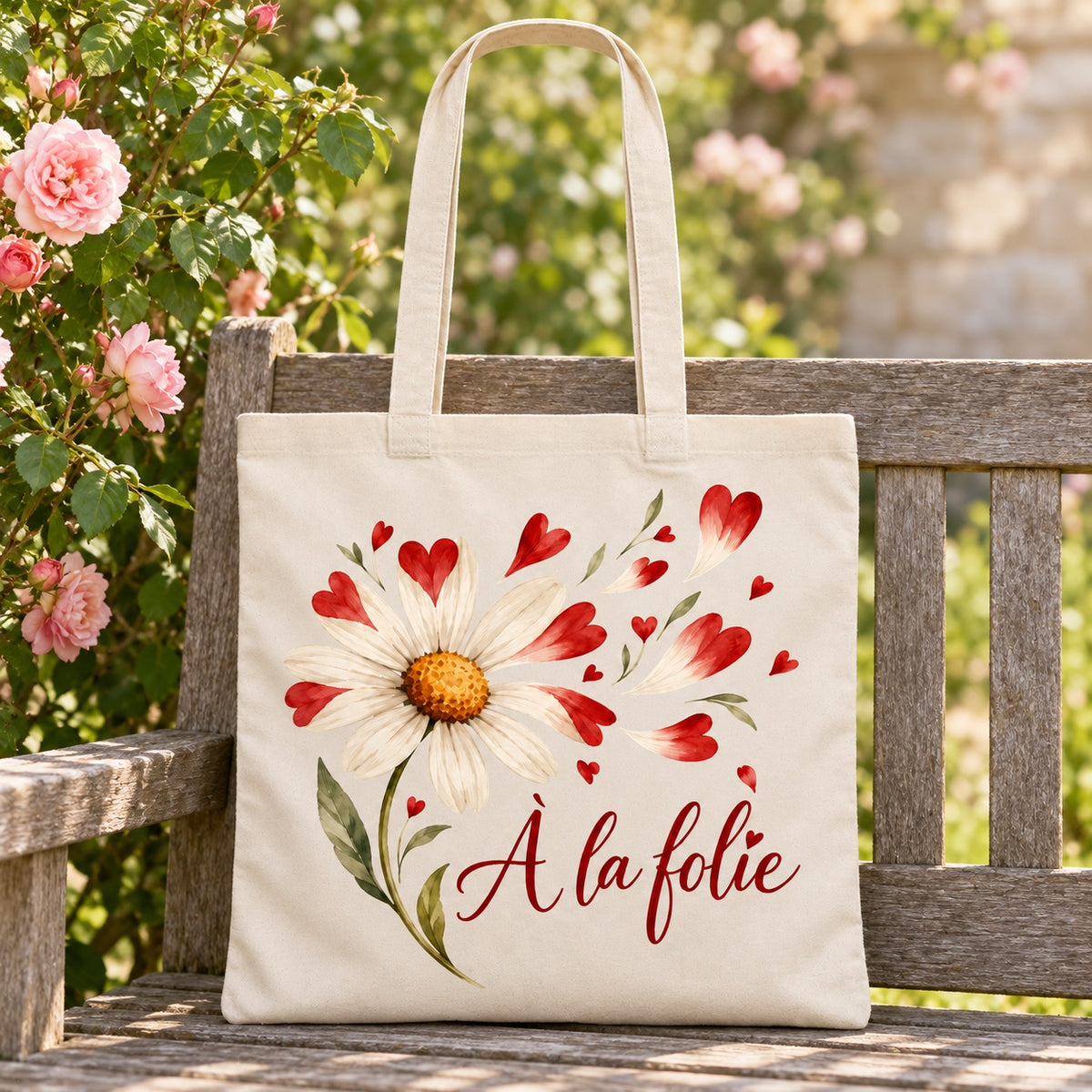 Tote bag « À la folie » Essentiel appuyé contre un banc de jardin près d'un rosier