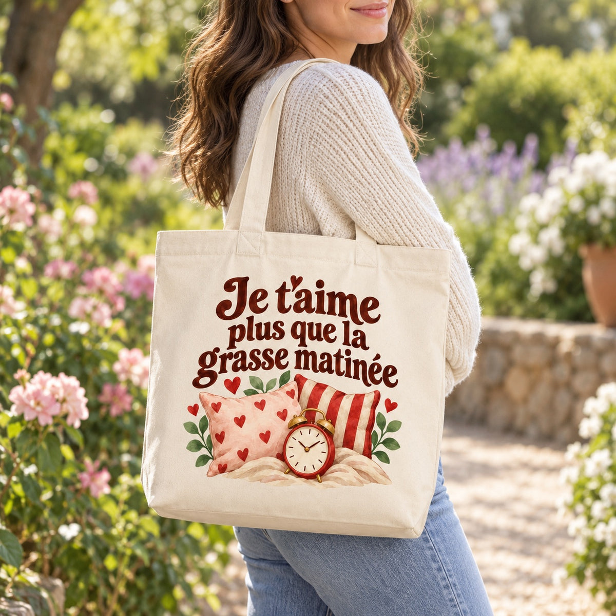Tote bag « Je t’aime plus que la grasse matinée » Premium porté à l'épaule dans un jardin fleuri