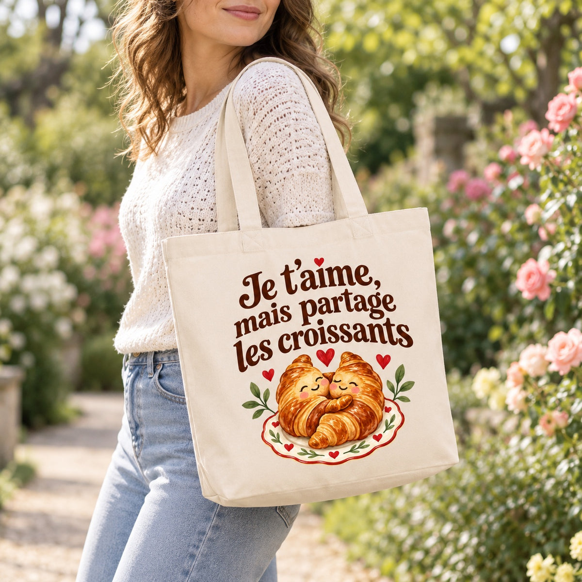 Tote bag « Je t’aime, mais partage les croissants » Premium porté à l'épaule dans un jardin fleuri