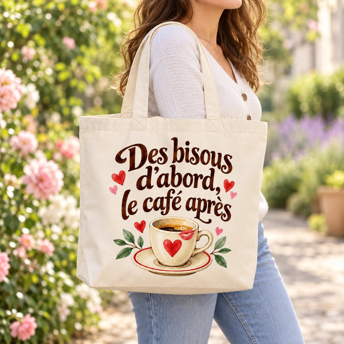 Tote bag « Des bisous d’abord, le café après » Premium porté à l'épaule dans un jardin fleuri