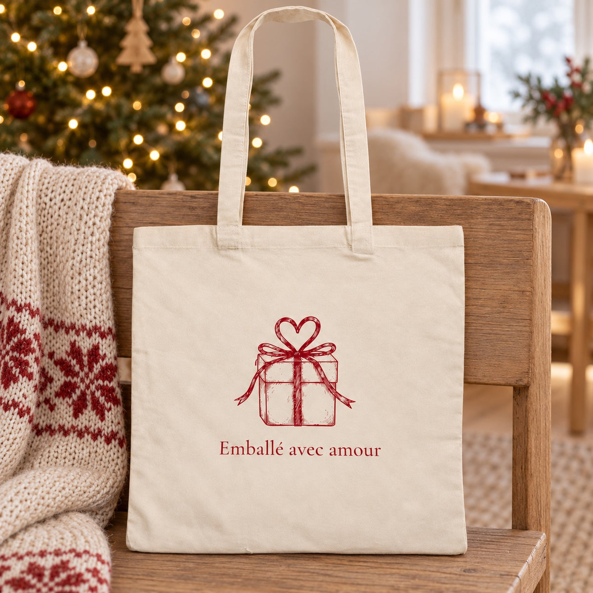 Tote bag de Noël « Emballé avec amour » Essentiel appuyé contre un banc près d'un plaid de Noël