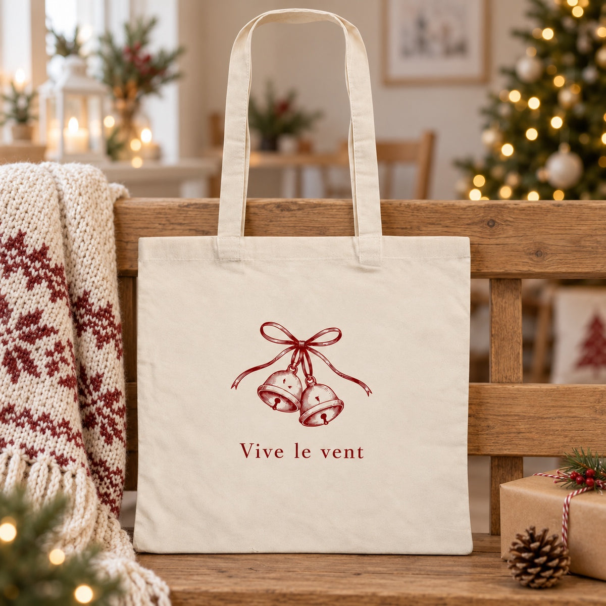 Tote bag de Noël « Vive le vent » Essentiel appuyé contre un banc près d'un plaid de Noël
