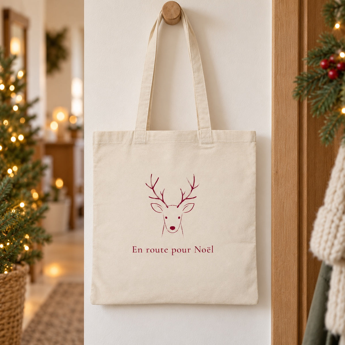 Tote bag de Noël « En route pour Noël » Essentiel suspendu à une patère dans une entrée décorée pour Noël