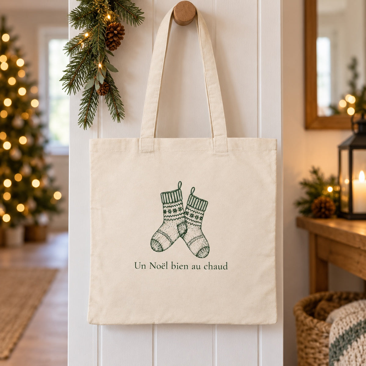 Tote bag de Noël « Un Noël bien au chaud » Essentiel suspendu à une patère dans une entrée décorée pour Noël