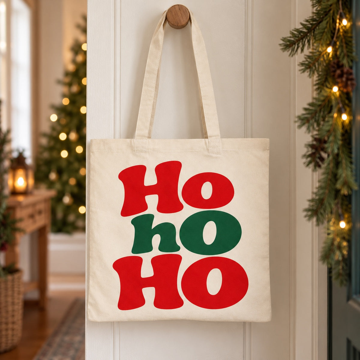Tote bag de Noël « Ho ho ho » Essentiel suspendu à une patère dans une entrée décorée pour Noël