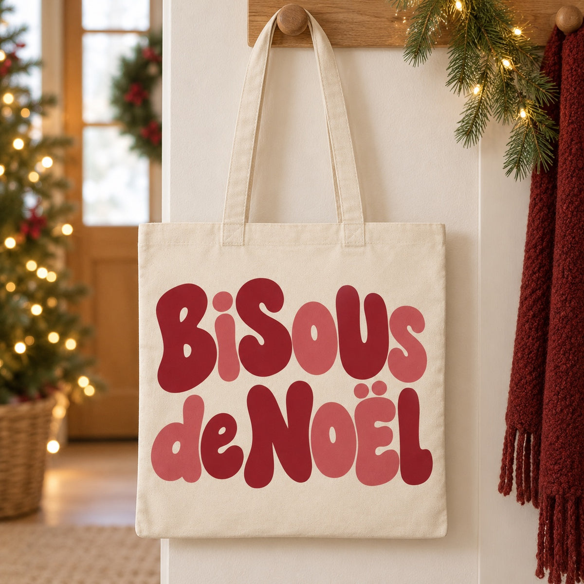 Tote bag de Noël « Bisous de Noël » Essentiel suspendu à une patère dans une entrée décorée pour Noël
