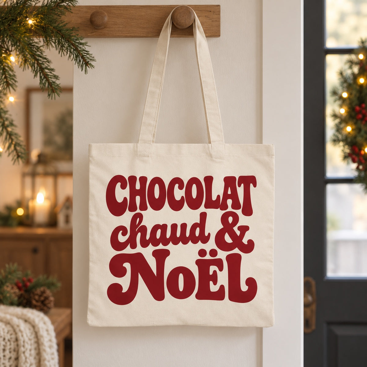 Tote bag de Noël « Chocolat chaud & Noël » Essentiel suspendu à une patère dans une entrée décorée pour Noël