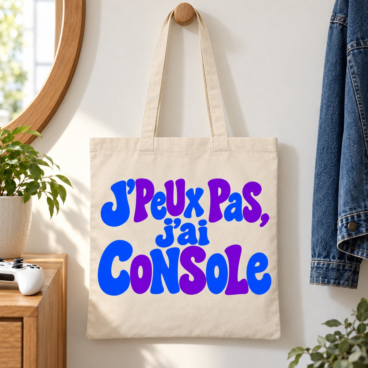 Tote bag « J'peux pas, j'ai console » Essentiel suspendu à une patère dans une entrée