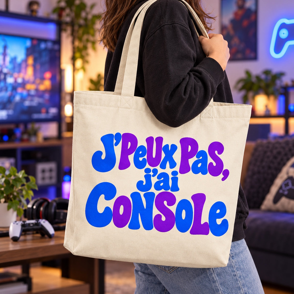 Tote bag « J'peux pas, j'ai console » Premium porté à l'épaule dans une salle de jeux aux néons