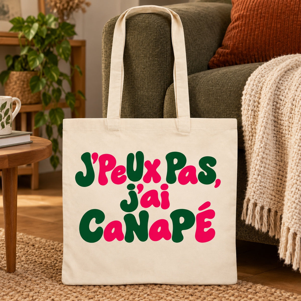 Tote bag « J'peux pas, j'ai canapé » Essentiel appuyé contre un canapé vert près d'un plaid