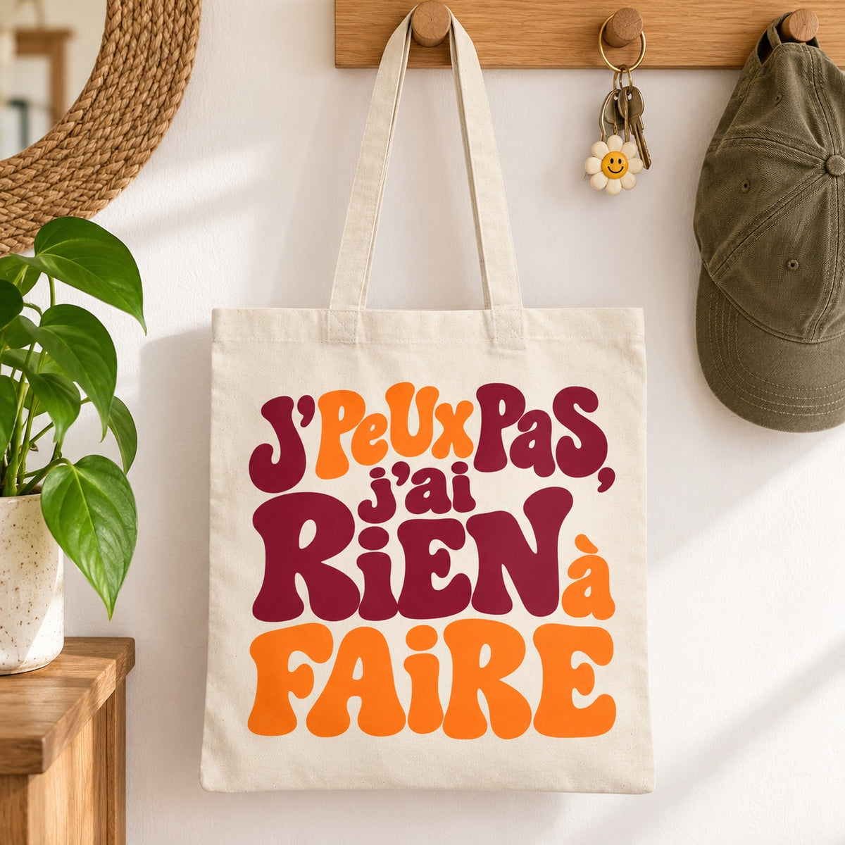 Tote bag « J'peux pas, j'ai rien à faire » Essentiel suspendu à une patère dans une entrée