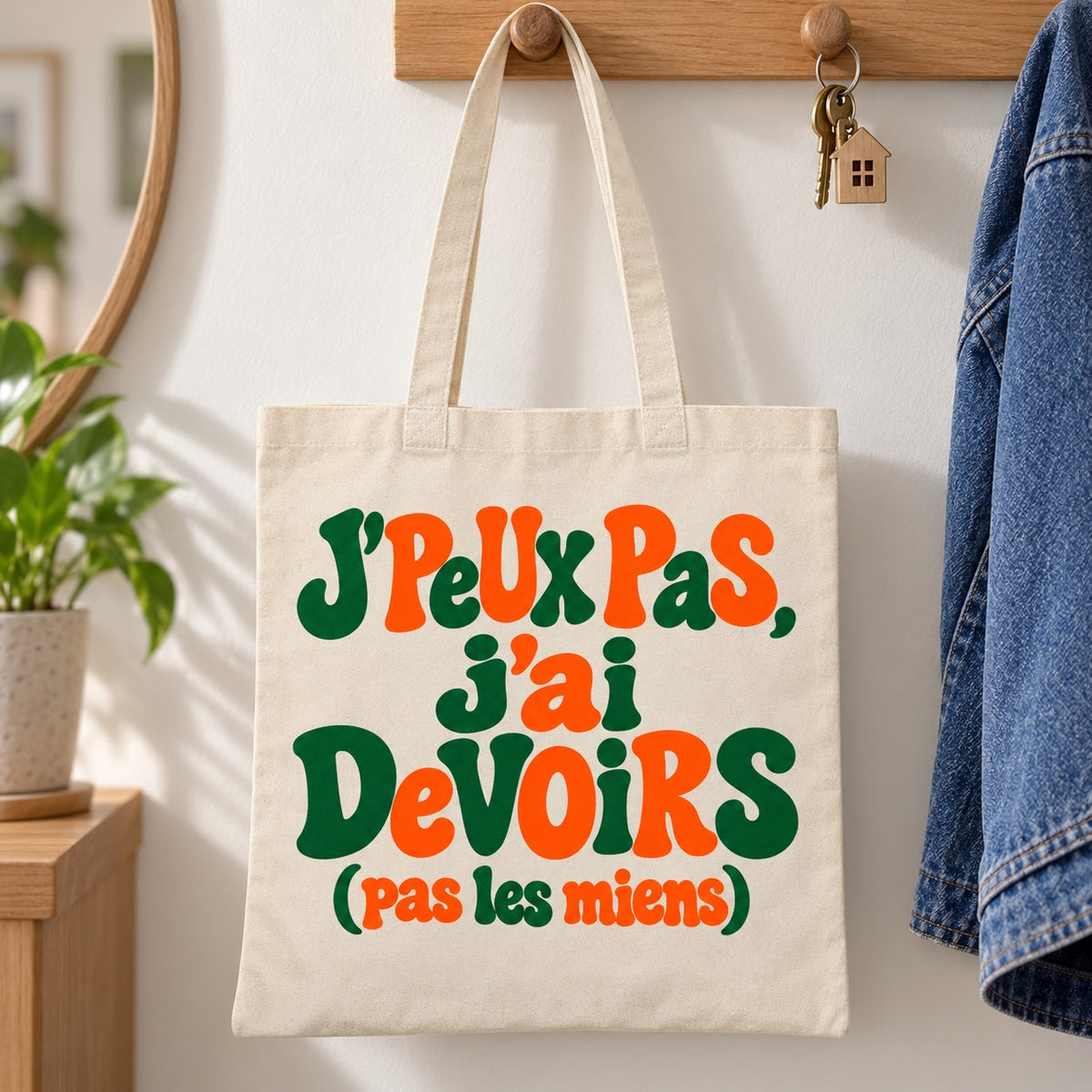 Tote bag « J'peux pas, j'ai devoirs (pas les miens) » Essentiel suspendu à une patère dans une entrée