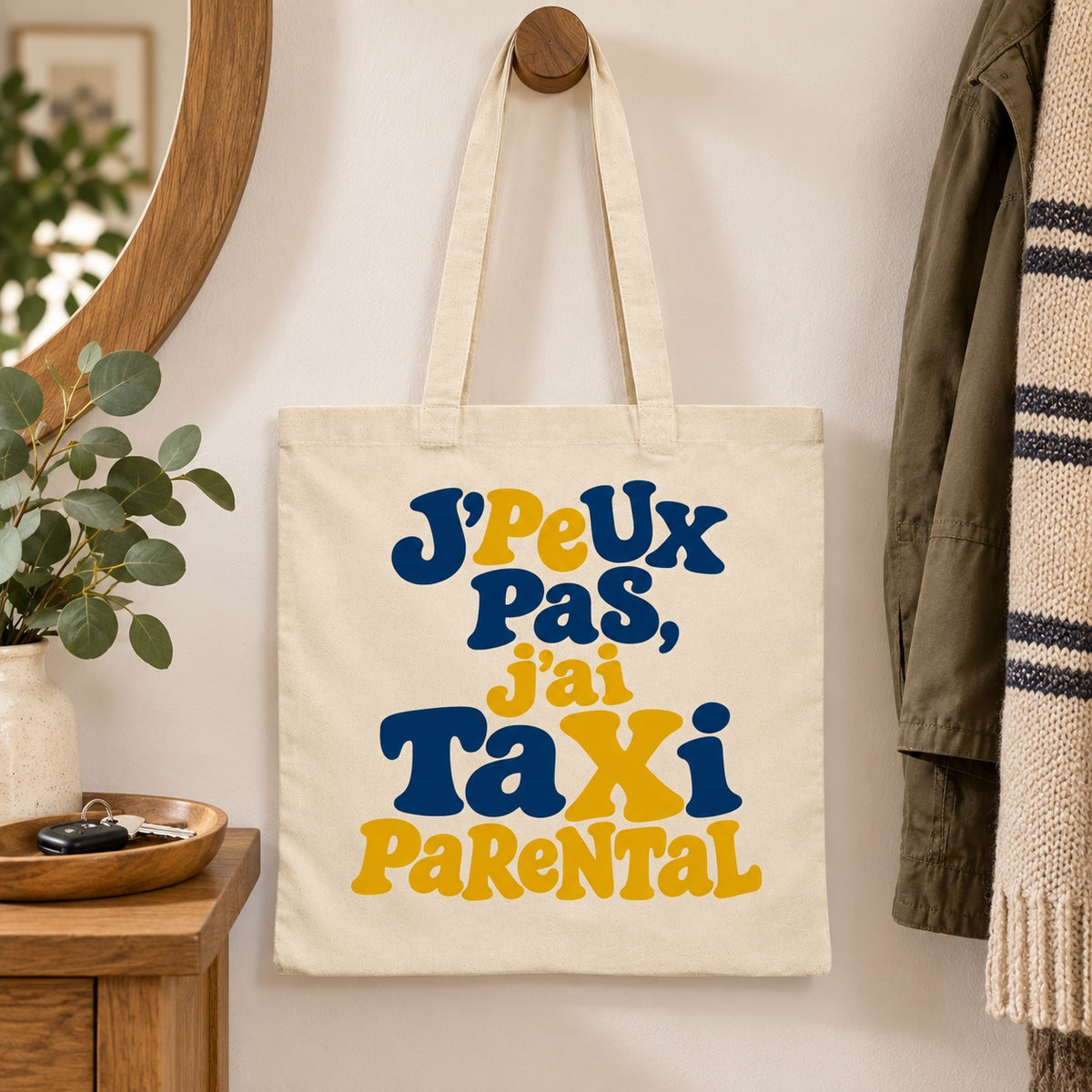 Tote bag « J'peux pas, j'ai taxi parental » Essentiel suspendu à une patère dans une entrée