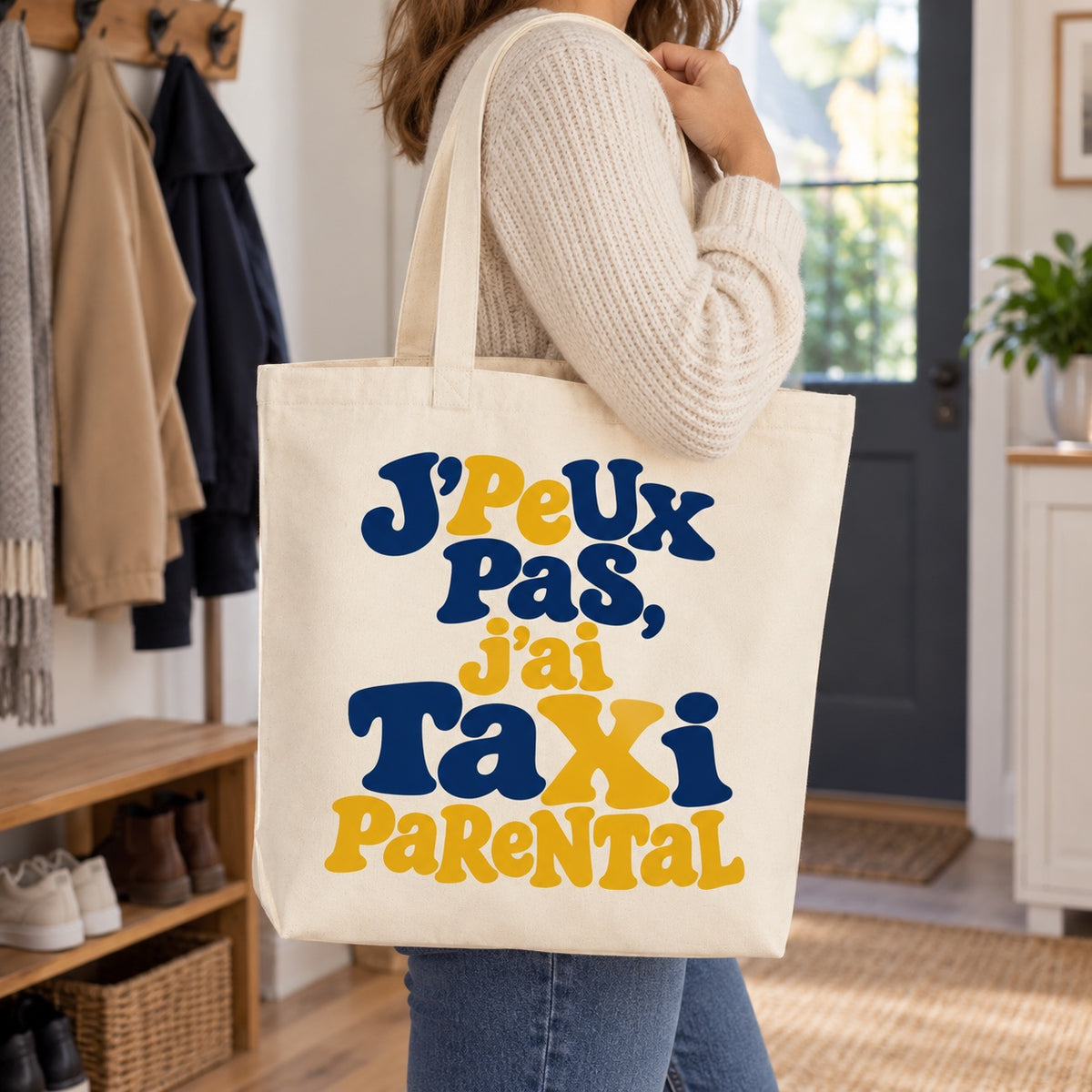 Tote bag « J'peux pas, j'ai taxi parental » Premium porté à l'épaule dans l'entrée d'une maison familiale