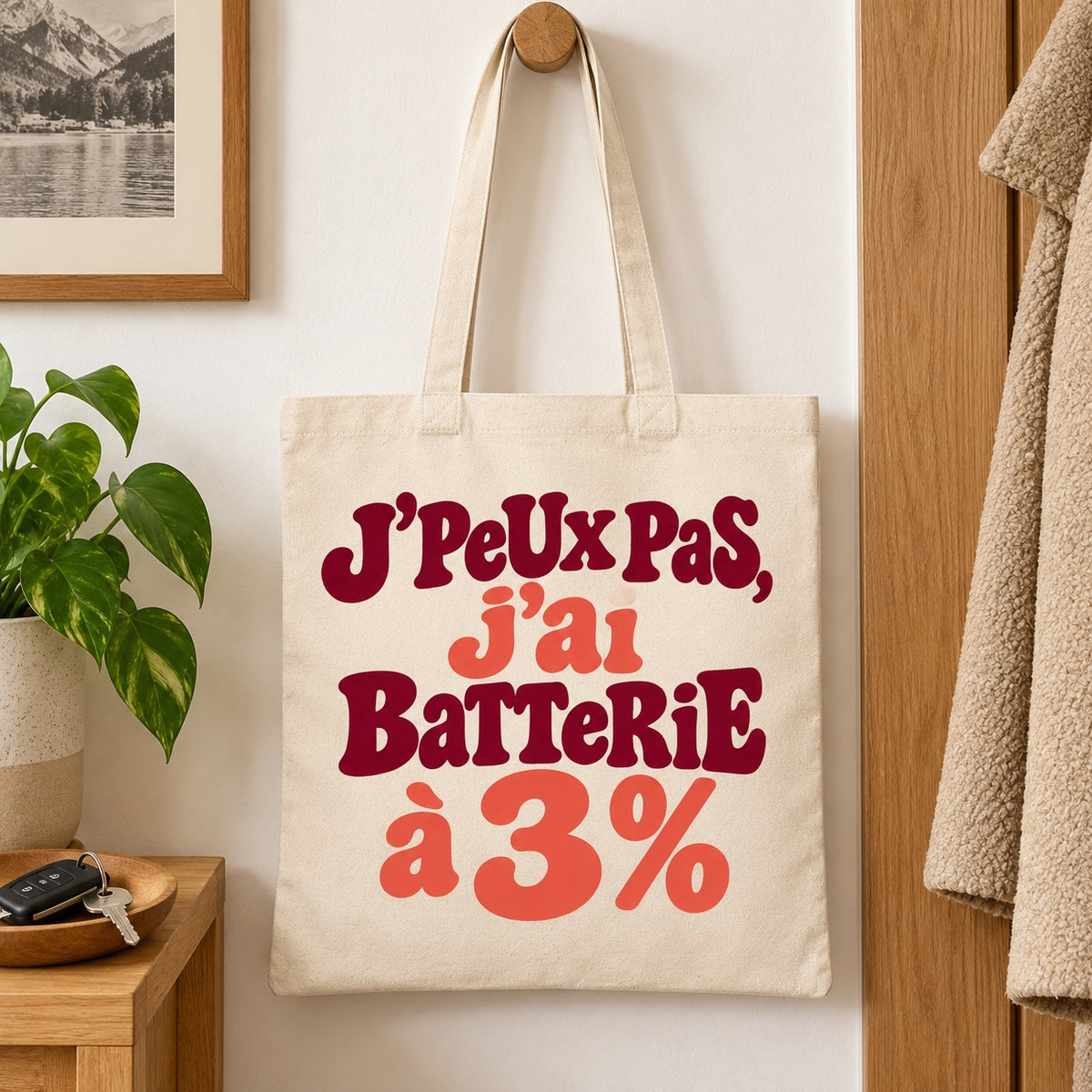 Tote bag « J'peux pas, j'ai batterie à 3 % » Essentiel suspendu à une patère dans une entrée