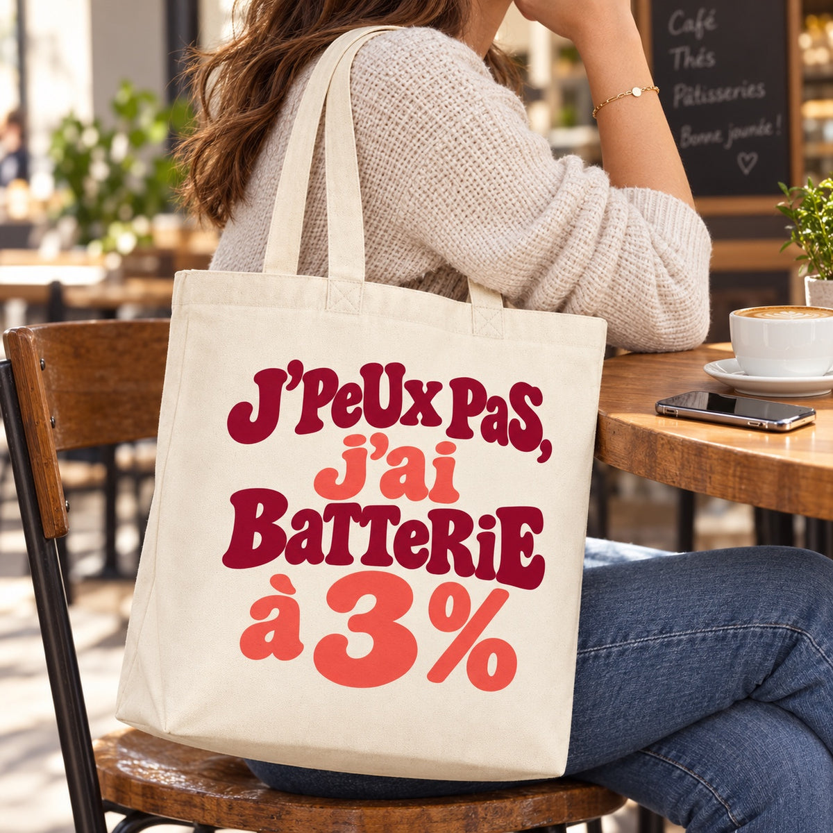 Tote bag « J'peux pas, j'ai batterie à 3 % » Premium porté à l'épaule à une terrasse de café
