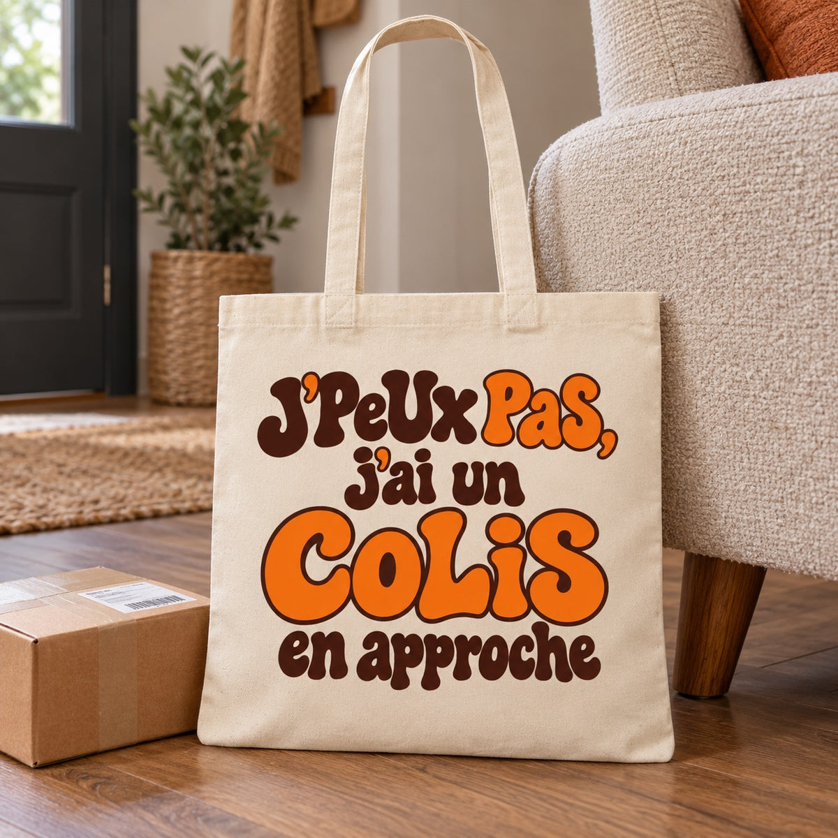 Tote bag « J'peux pas, j'ai un colis en approche » Essentiel appuyé contre un fauteuil d'entrée près d'un colis