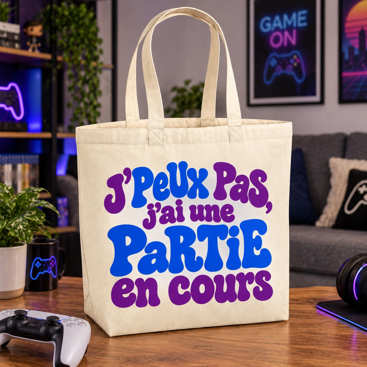 Tote bag « J'peux pas, j'ai une partie en cours » Premium posé sur une table basse près d'une manette