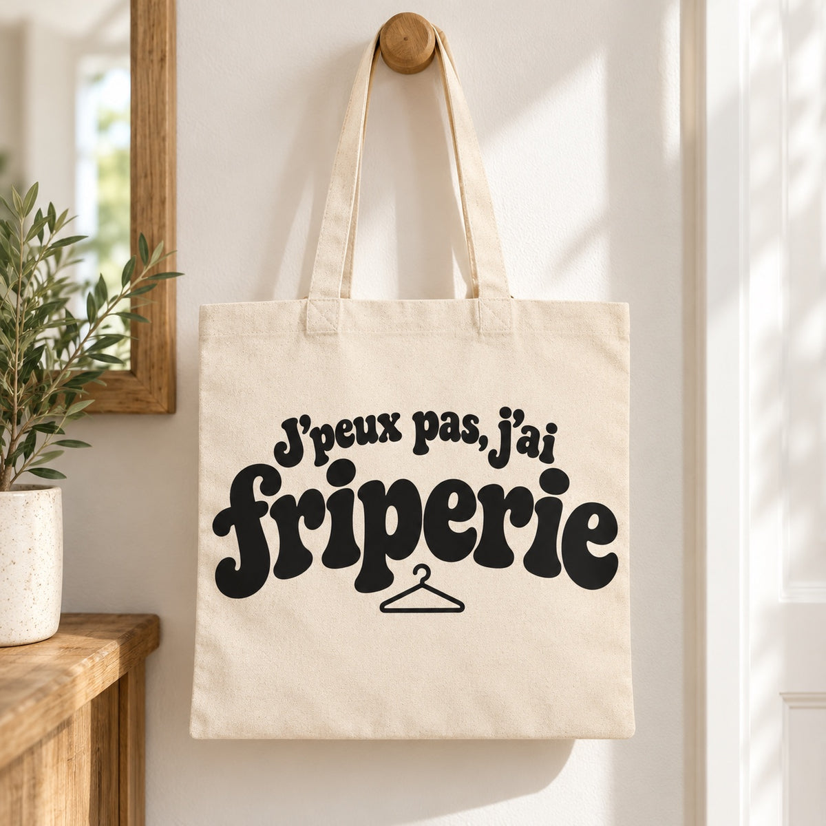 Tote bag « J'peux pas, j'ai friperie » Essentiel suspendu à une patère dans une entrée lumineuse