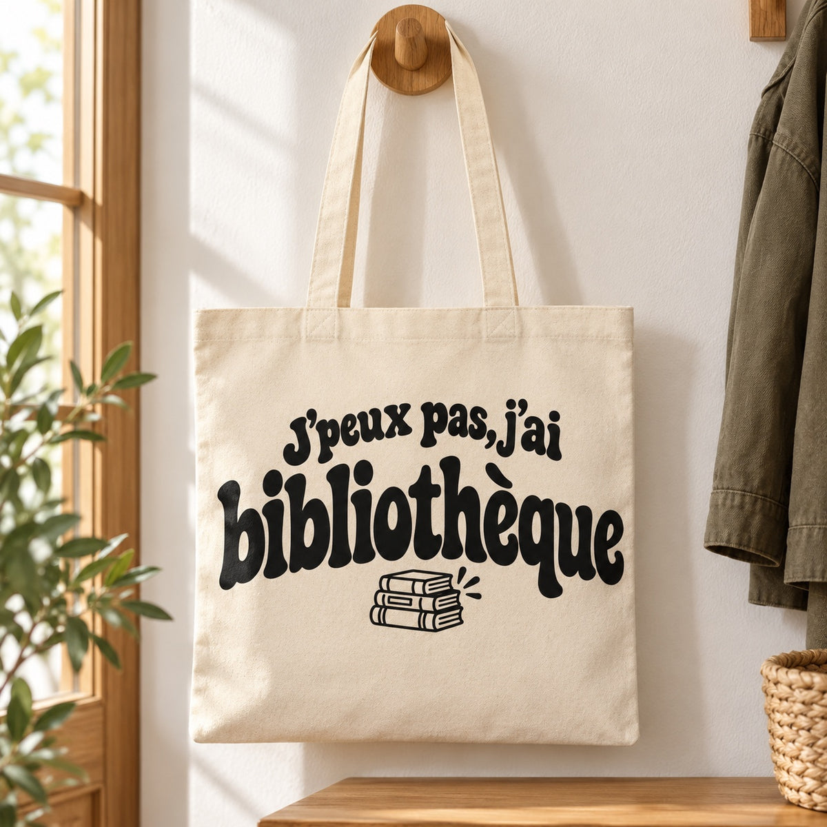 Tote bag « J'peux pas, j'ai bibliothèque » Essentiel suspendu à une patère dans une entrée lumineuse