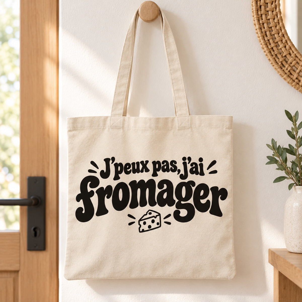Tote bag « J'peux pas, j'ai fromager » Essentiel suspendu à une patère dans une entrée lumineuse