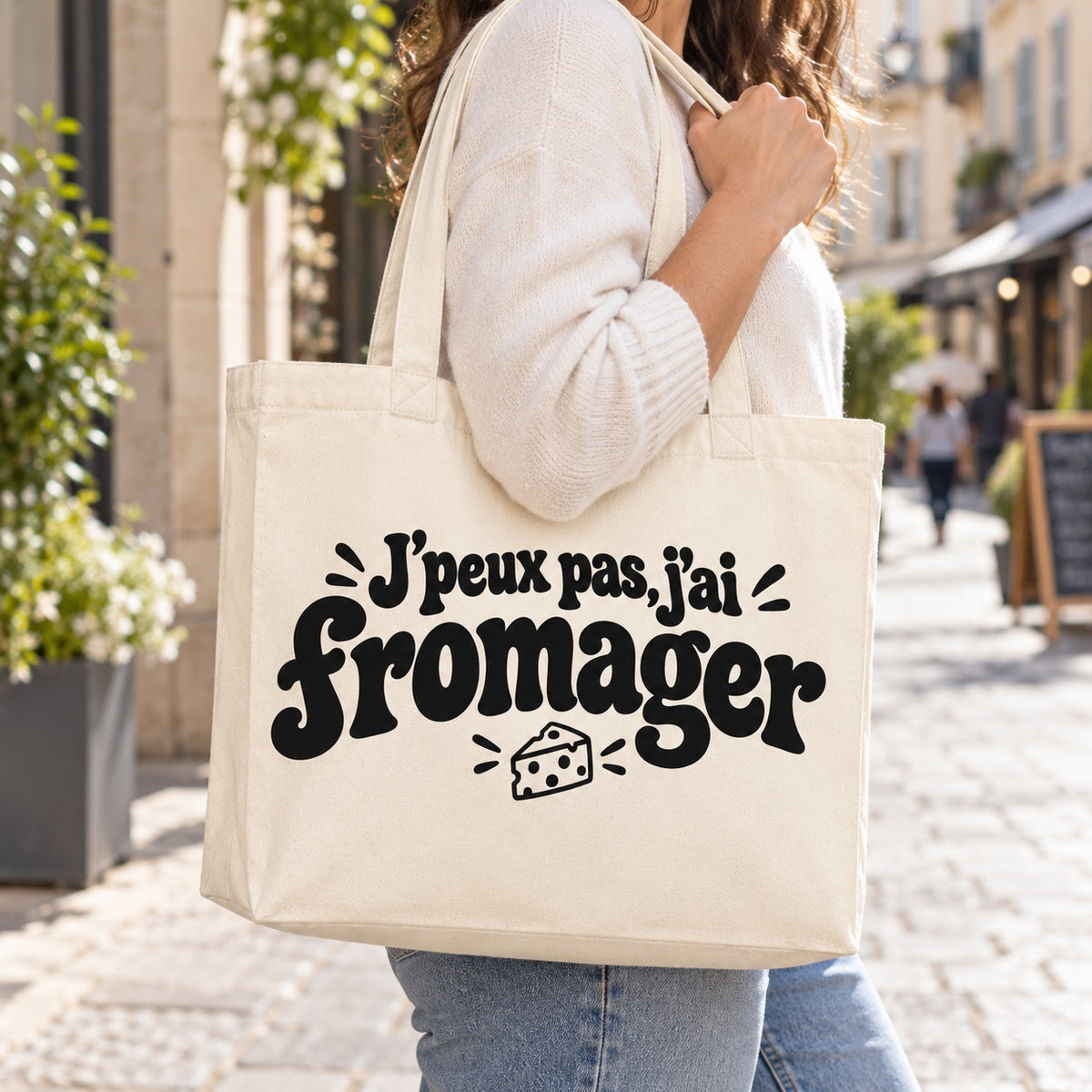 Tote bag « J'peux pas, j'ai fromager » Premium porté à l'épaule dans une rue piétonne ensoleillée