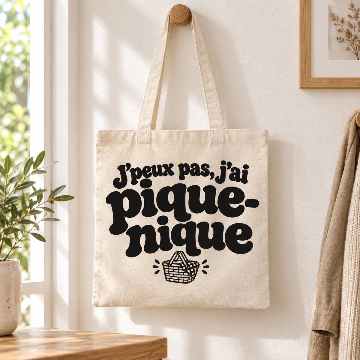 Tote bag « J'peux pas, j'ai pique-nique » Essentiel suspendu à une patère dans une entrée lumineuse
