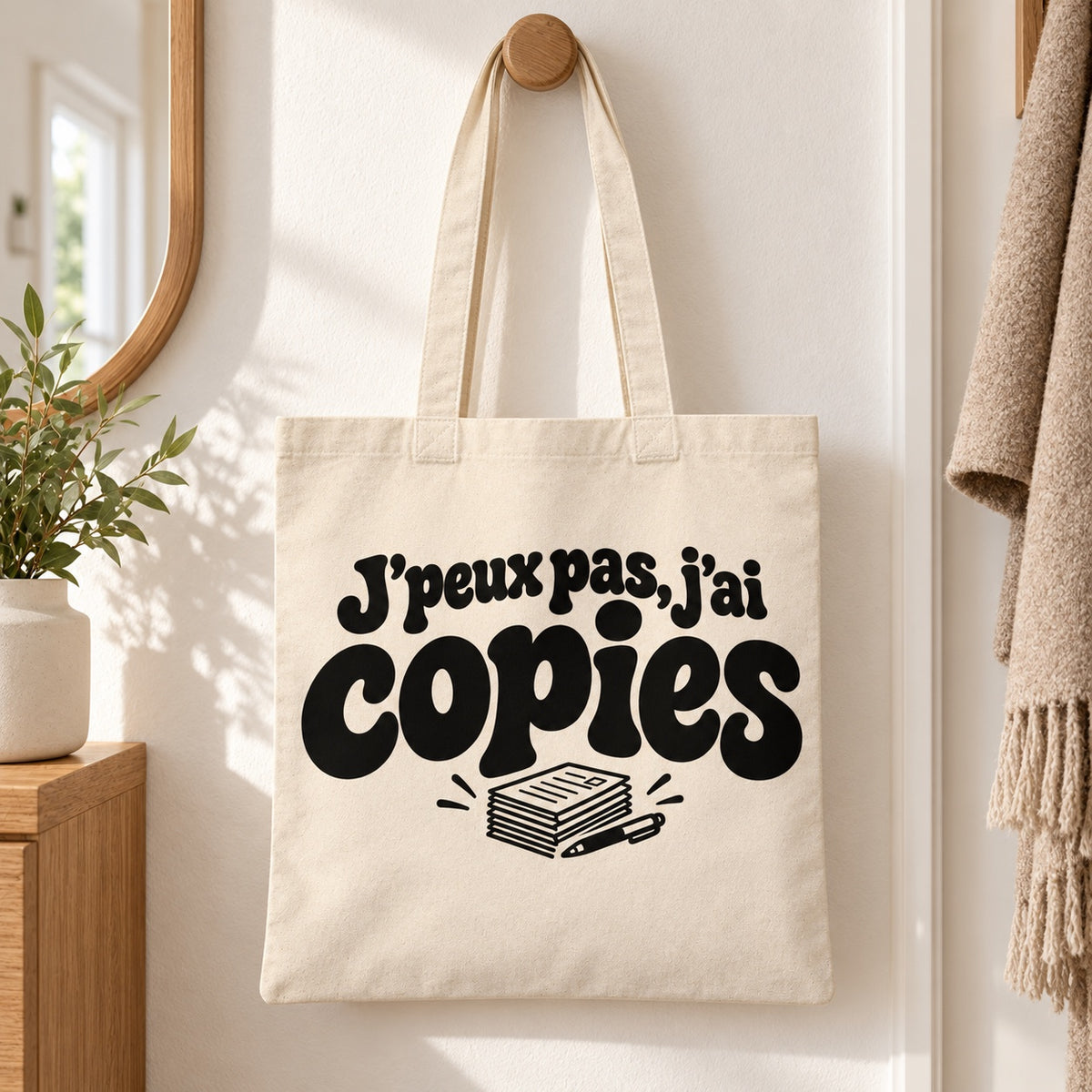 Tote bag « J'peux pas, j'ai copies » Essentiel suspendu à une patère dans une entrée lumineuse