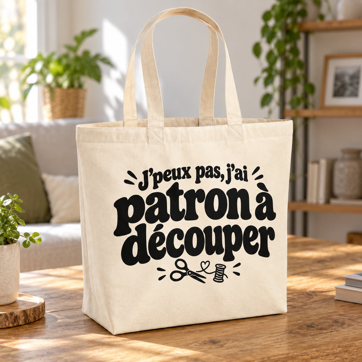 Tote bag « J'peux pas, j'ai patron à découper » Premium posé sur une table en bois dans un salon lumineux