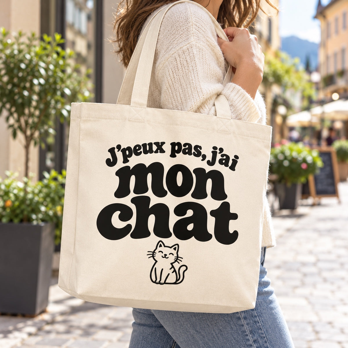 Tote bag « J'peux pas, j'ai mon chat » Premium porté à l'épaule dans une rue piétonne ensoleillée