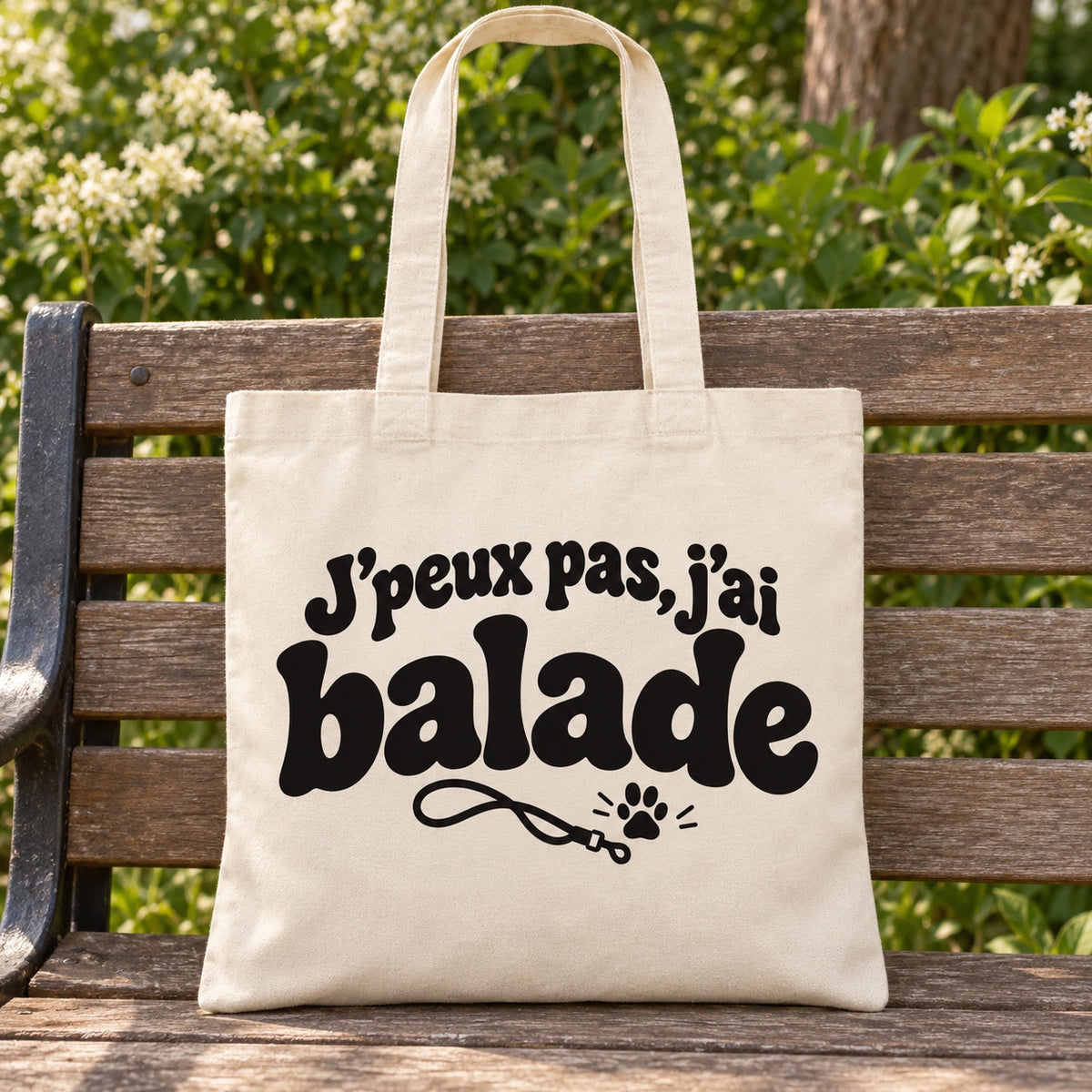 Tote bag « J'peux pas, j'ai balade » Essentiel posé sur un banc en bois dans un jardin