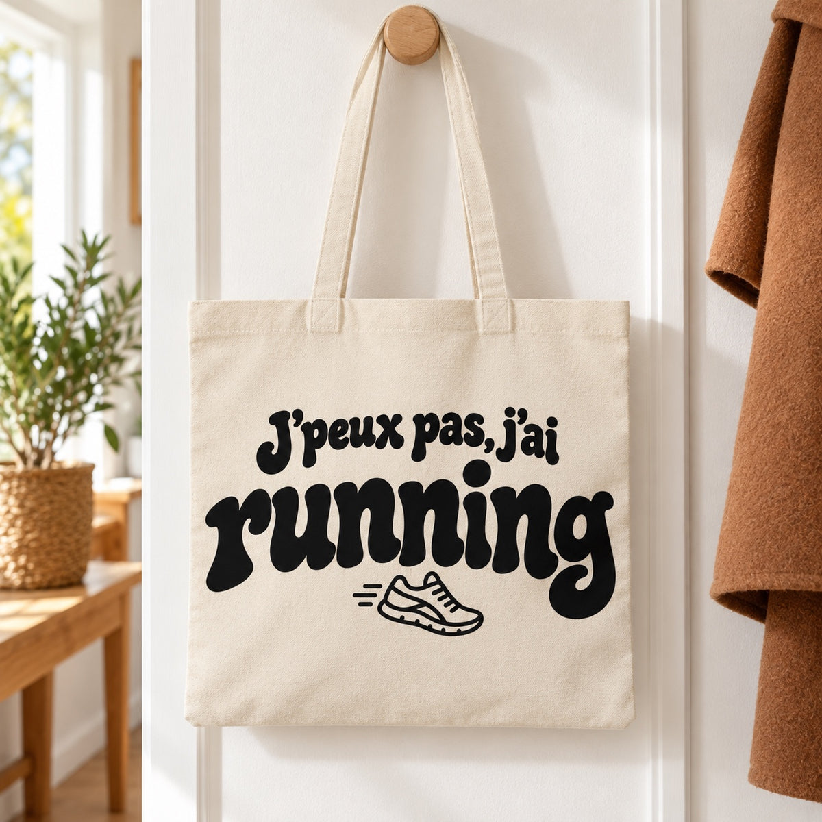 Tote bag « J'peux pas, j'ai running » Essentiel suspendu à une patère dans une entrée lumineuse