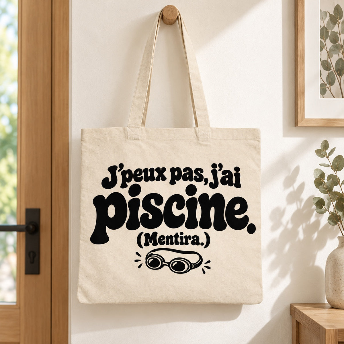 Tote bag « J'peux pas, j'ai piscine. (Mentira.) » Essentiel suspendu à une patère dans une entrée lumineuse